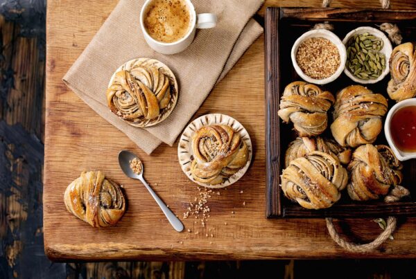 Traditional Swedish cardamom sweet buns Kanelbulle in wooden tray, cup of coffee, ingredients in ceramic bowl above on wooden table